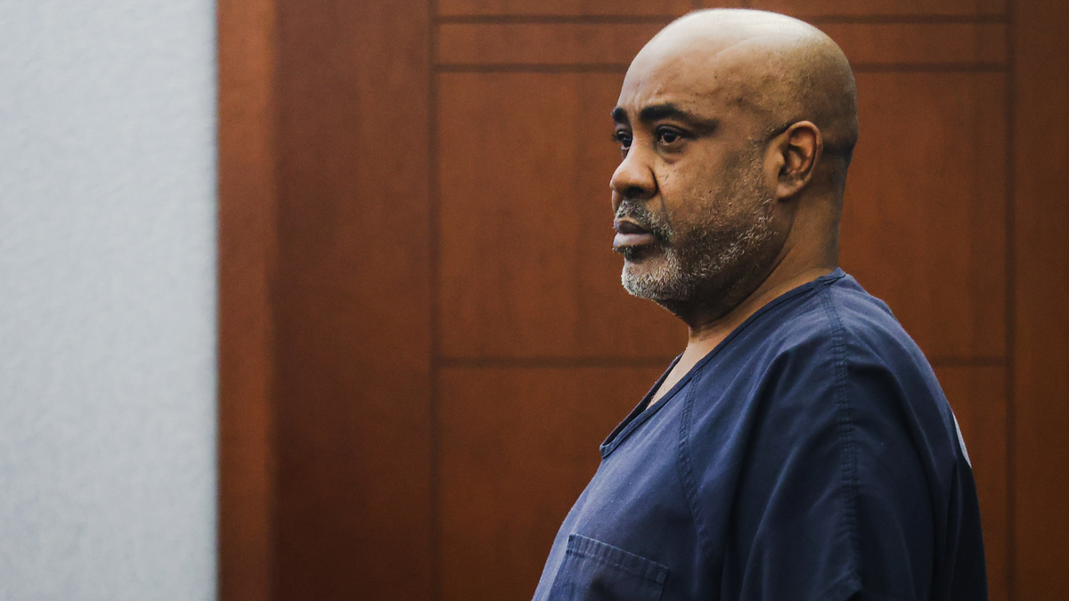 A man stands in a courtroom wearing a dark outfit. The image lacks specific context or identifiable details for categorization