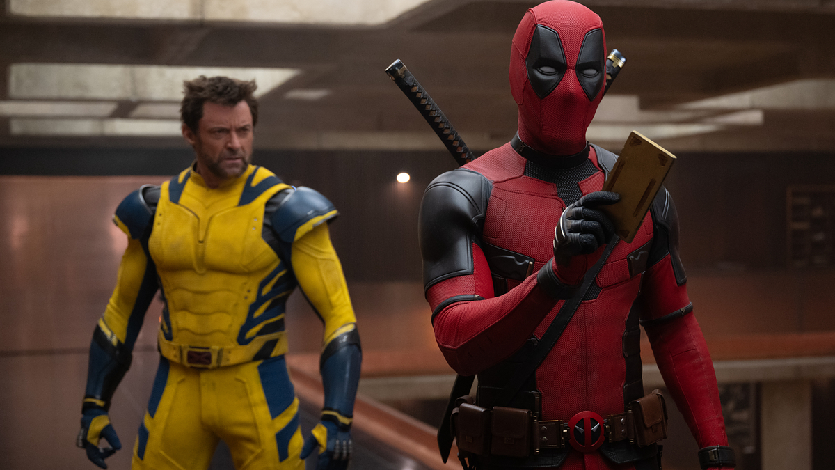 Deadpool looks at his phone while Wolverine stands behind him in a futuristic setting. Deadpool wears his signature suit, and Wolverine is in a yellow and blue costume