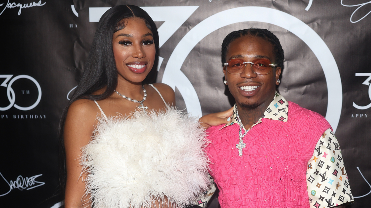 Yung Miami in a feathered outfit and Jacquees in a pink Louis Vuitton vest pose on the red carpet at a 30th birthday event