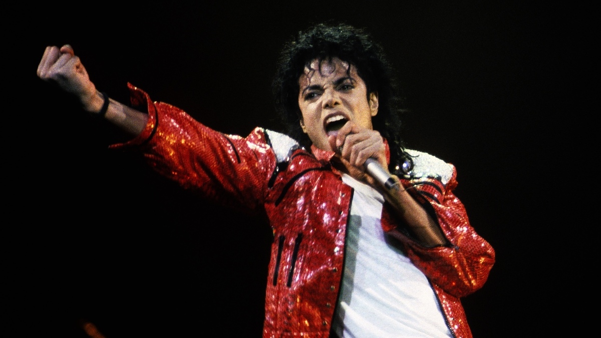 Michael Jackson performs on stage, wearing a sparkling jacket and passionately singing into a microphone