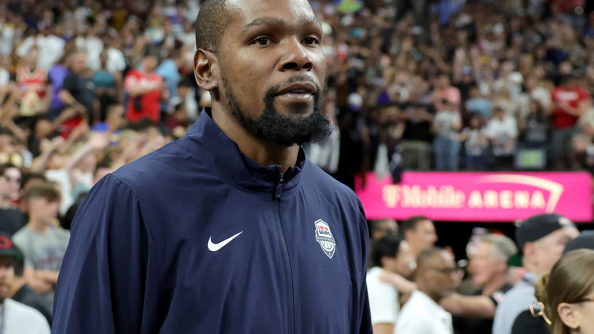 Kevin Durant in a USA team tracksuit at an indoor sports event, with a crowded audience in the background
