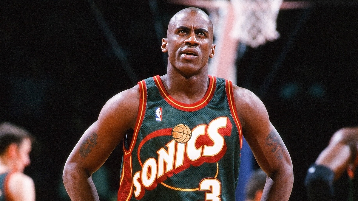 A basketball player in a Seattle SuperSonics jersey stands on the court with hands on hips, looking upwards