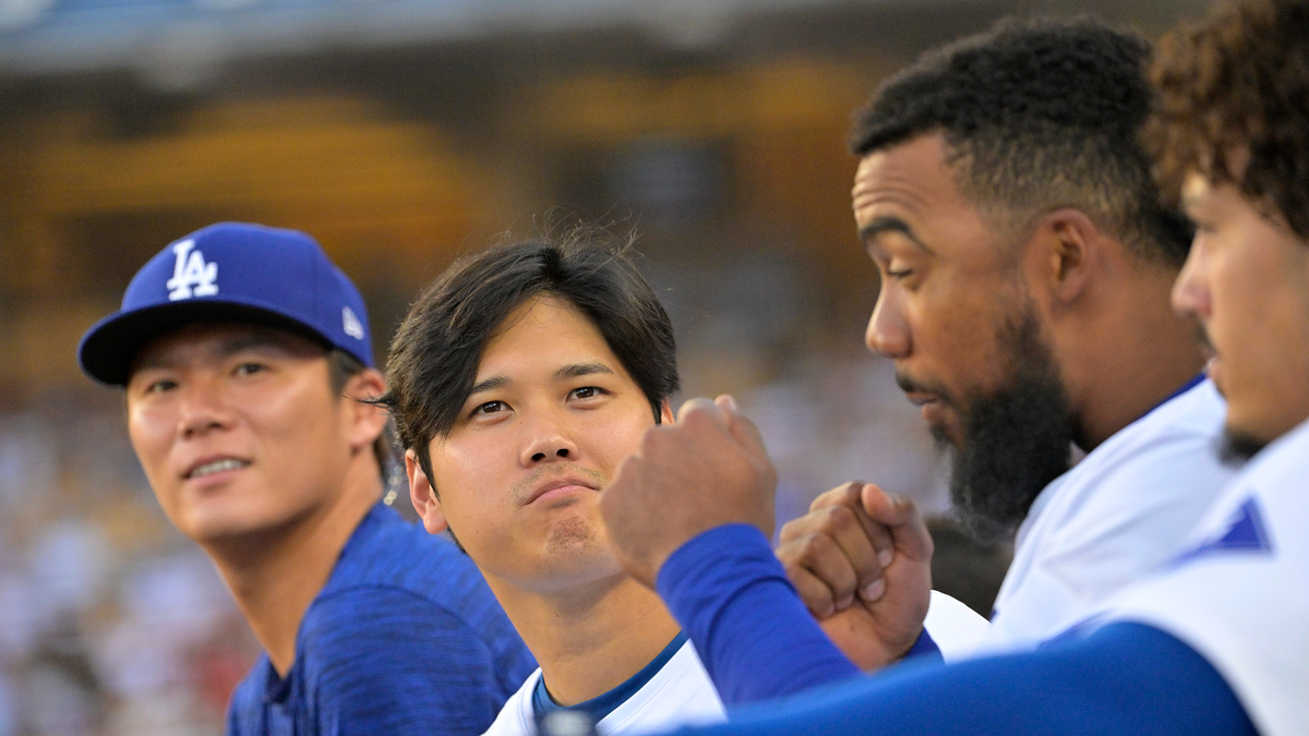 Hyun Jin Ryu, Shohei Ohtani, and two teammates sit on the bench during a baseball game, engaged in conversation and showing camaraderie