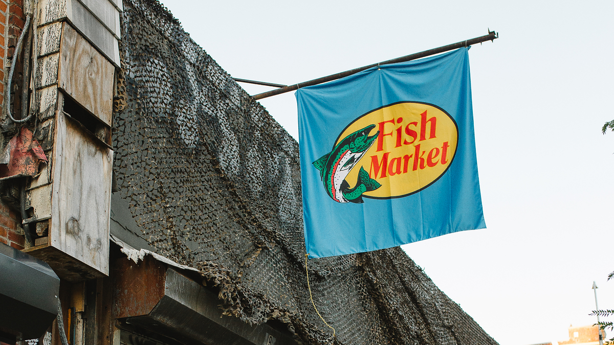 An exterior shot of the Fish Market, featuring a camouflage net covering the building and a bright blue sign with "Fish Market" hanging above the entrance