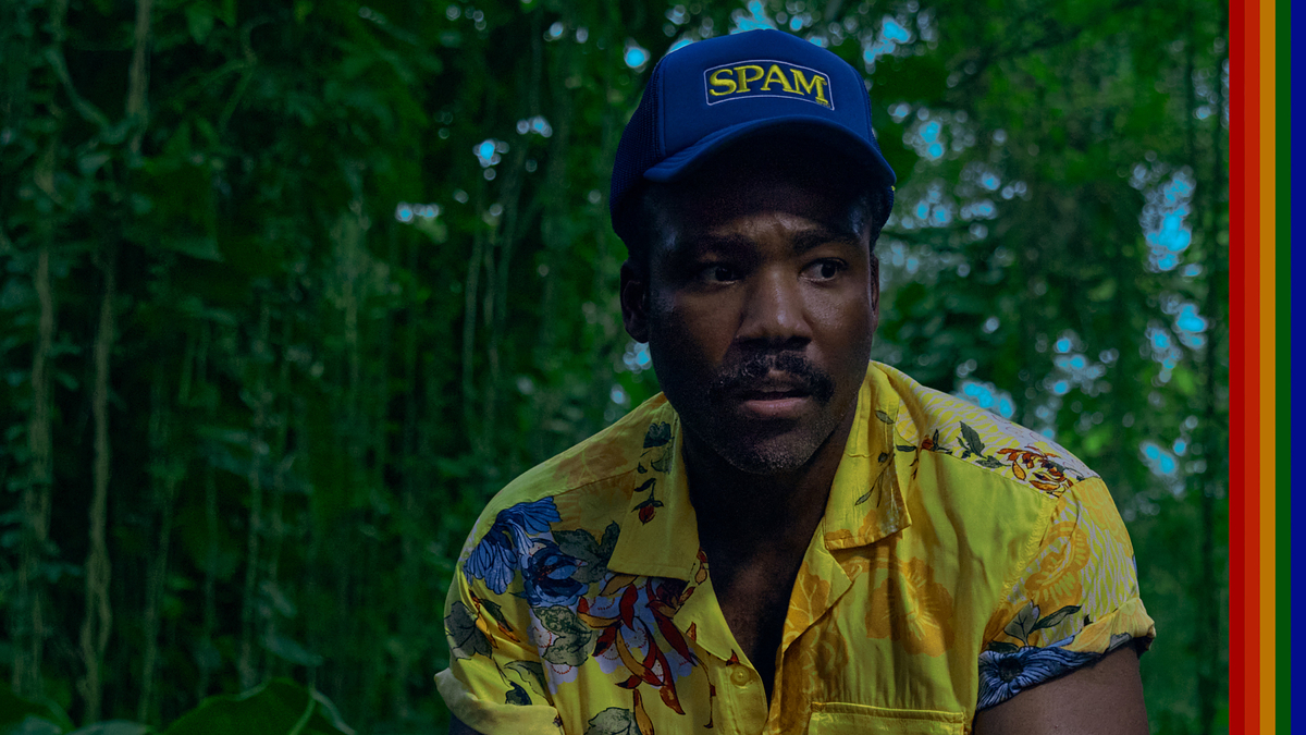Donald Glover wearing a colorful floral shirt and a "SPAM" cap, standing in a lush, green jungle