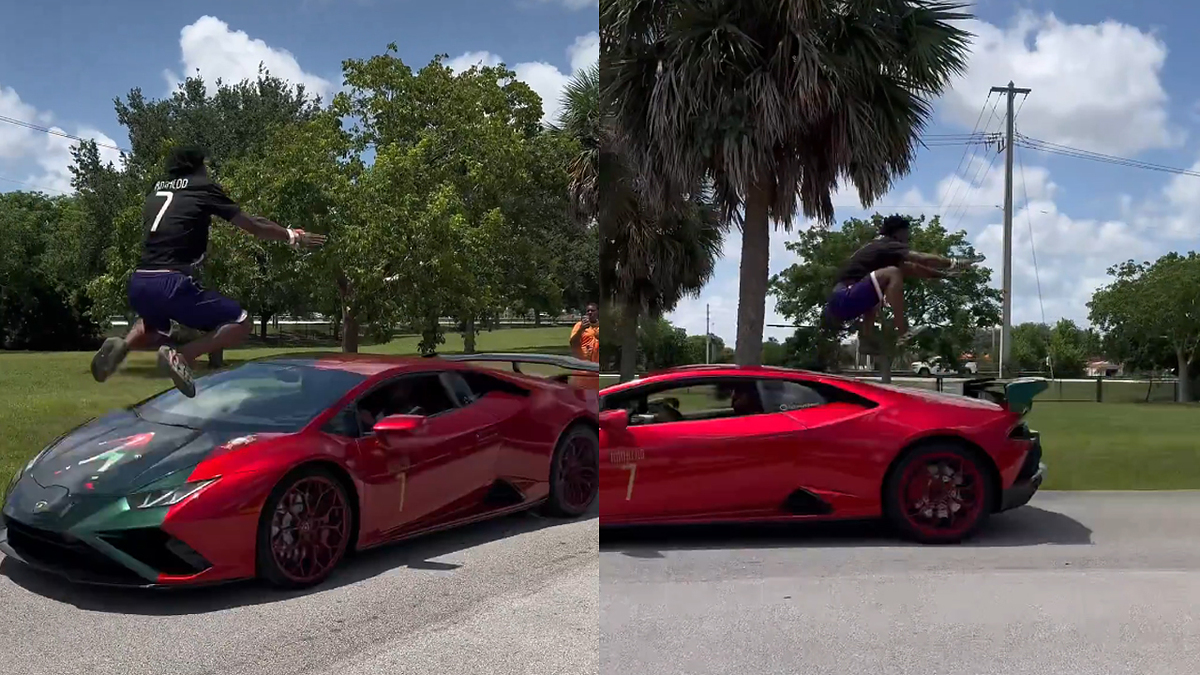 Person in shorts and a jersey with the number 7 jumps over a red sports car parked on a street in a park with trees and a palm tree in the background