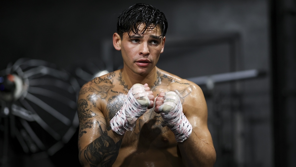 A shirtless man with multiple tattoos and wrapped fists stands in a boxing stance