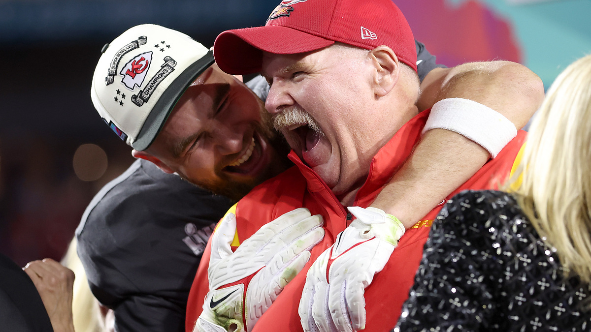 Travis Kelce and Andy Reid of the Kansas City Chiefs celebrate joyfully after a game. Travis is hugging Andy, who is wearing a red jacket and cap