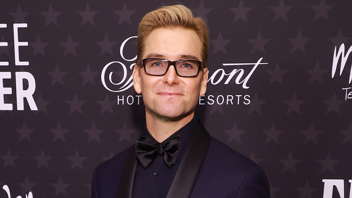 Man wearing glasses and a black tuxedo with a black bow tie poses in front of a backdrop featuring the Fairmont Hotels and Resorts logo