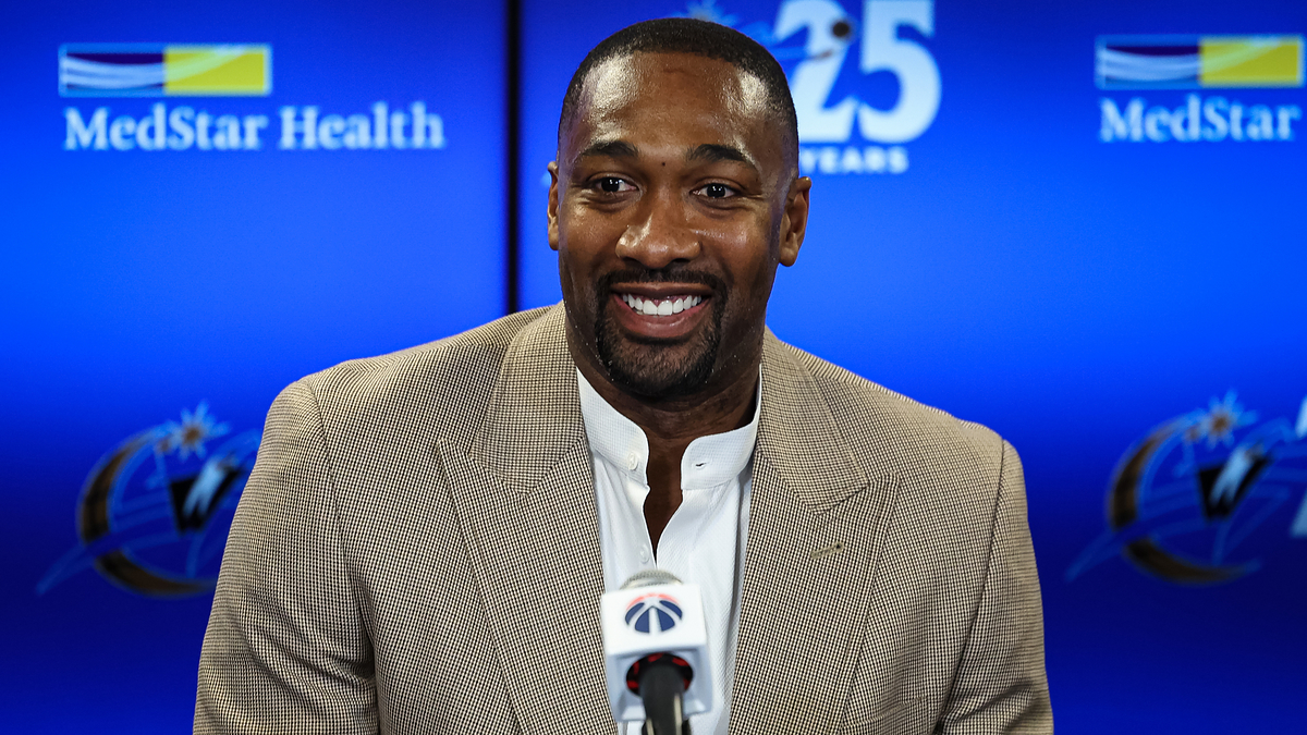 Gilbert Arenas smiles during a press conference with a MedStar Health banner and Washington Wizards logo in the background