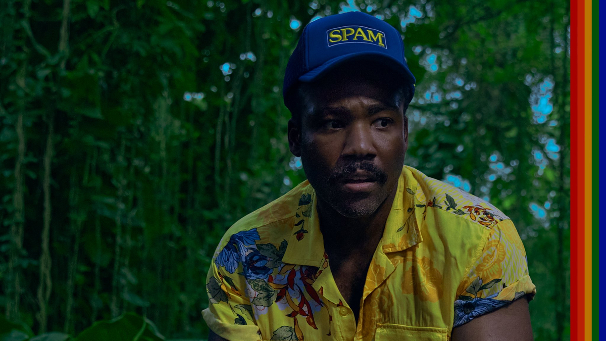 Donald Glover wearing a floral shirt and a blue "SPAM" hat, in a lush, green setting
