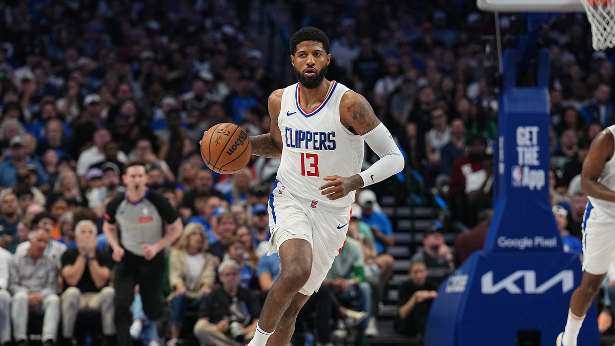 Paul George dribbles a basketball during an LA Clippers game, wearing his team uniform. A crowded arena and other players are seen in the background