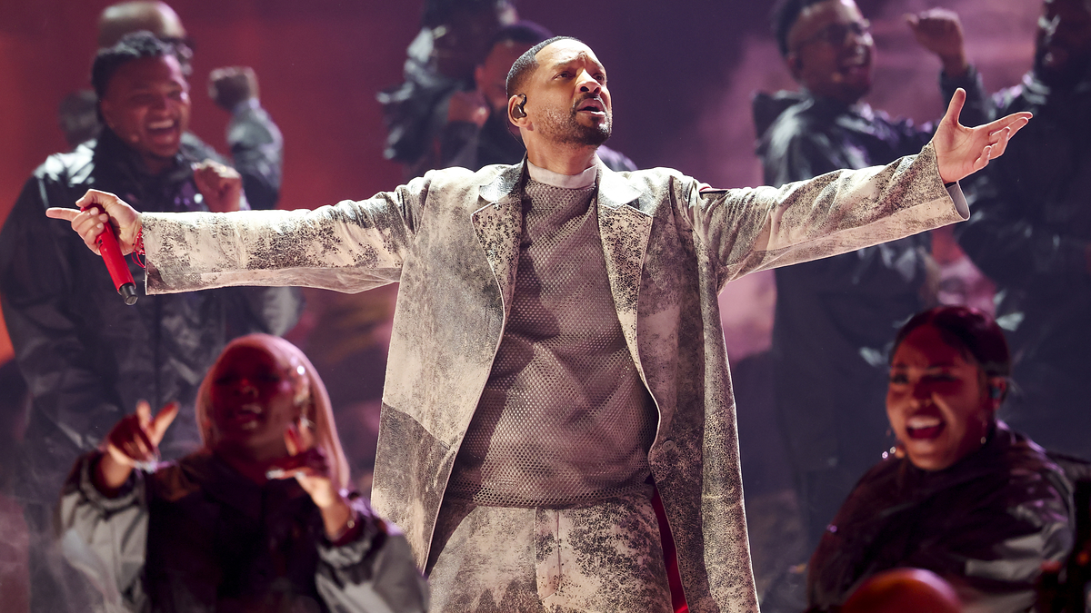 Will Smith performs on stage in an elaborate suit while backup singers in dark outfits sing enthusiastically behind him