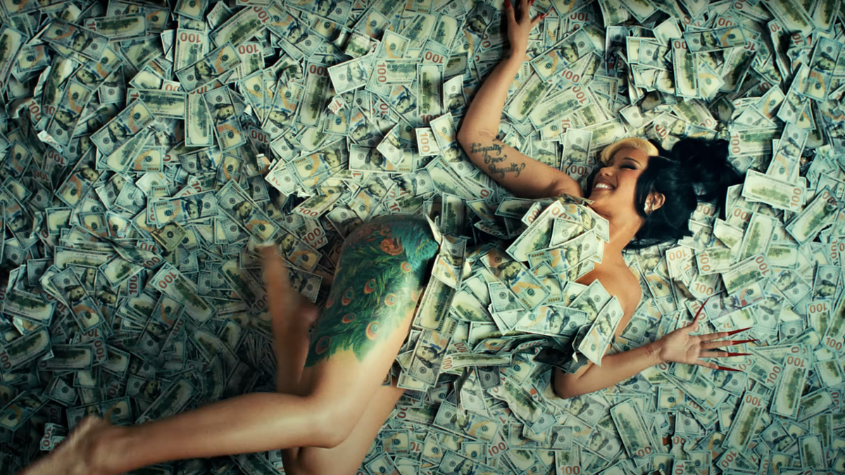 A person with tattoos, lying joyfully on a large pile of dollar bills, smiling at the camera