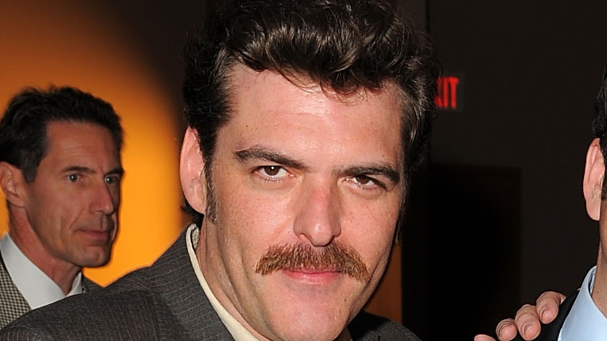 Actor Jay Johnston in the foreground and another man in a suit in the background at an indoor event