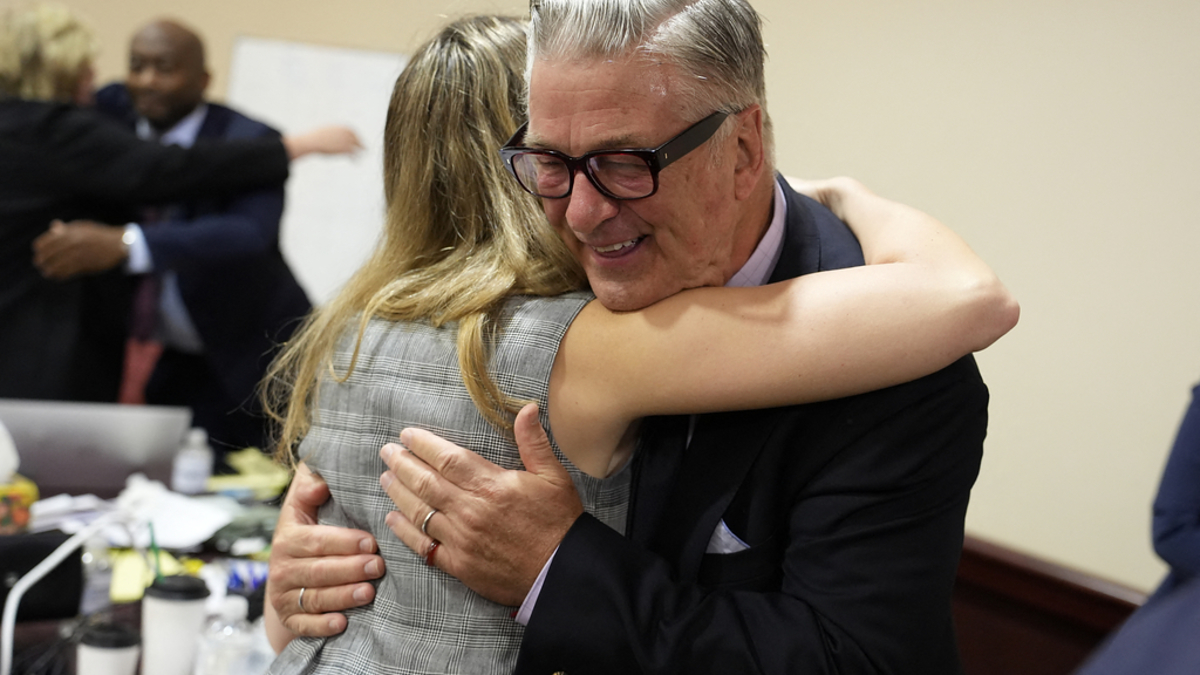 Alec Baldwin hugs a woman in a professional setting, both appearing happy and engaged in conversation