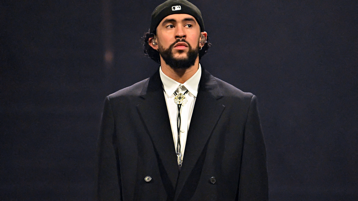 Bad Bunny wears a black blazer and a black backward cap during a public appearance