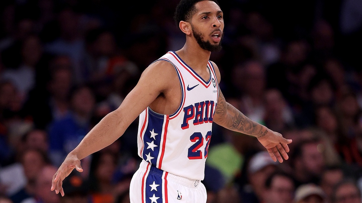 A basketball player wearing a Philadelphia 76ers jersey with the number 22 is on the court, with an audience in the background