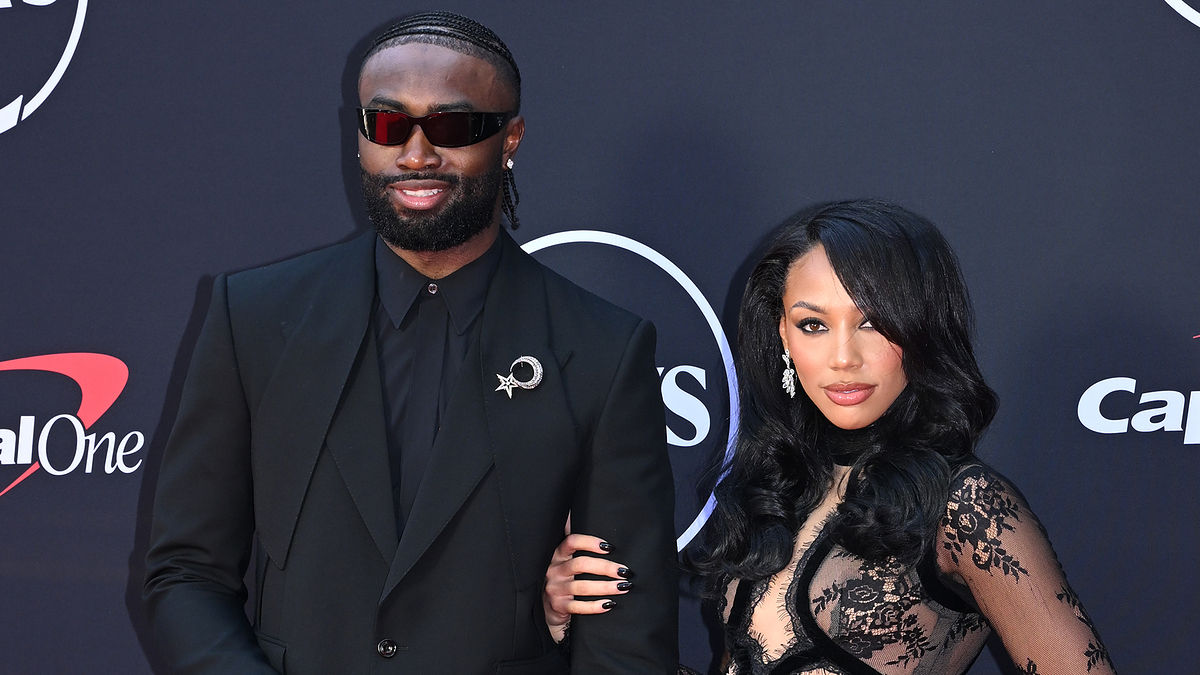 Jaylen Brown and Bernice Burgos pose on the red carpet. Jaylen is in a black suit with dark sunglasses, Bernice wears a see-through black lace dress