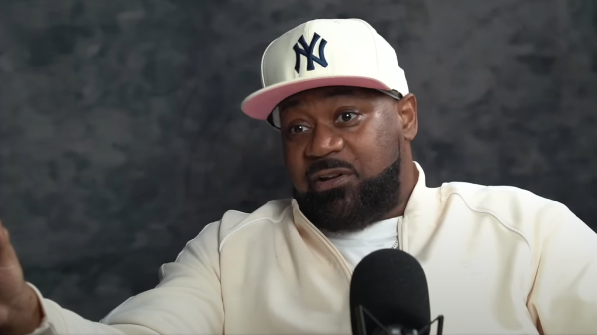 Ghostface Killah wearing a white jacket and a New York Yankees cap, speaking into a microphone