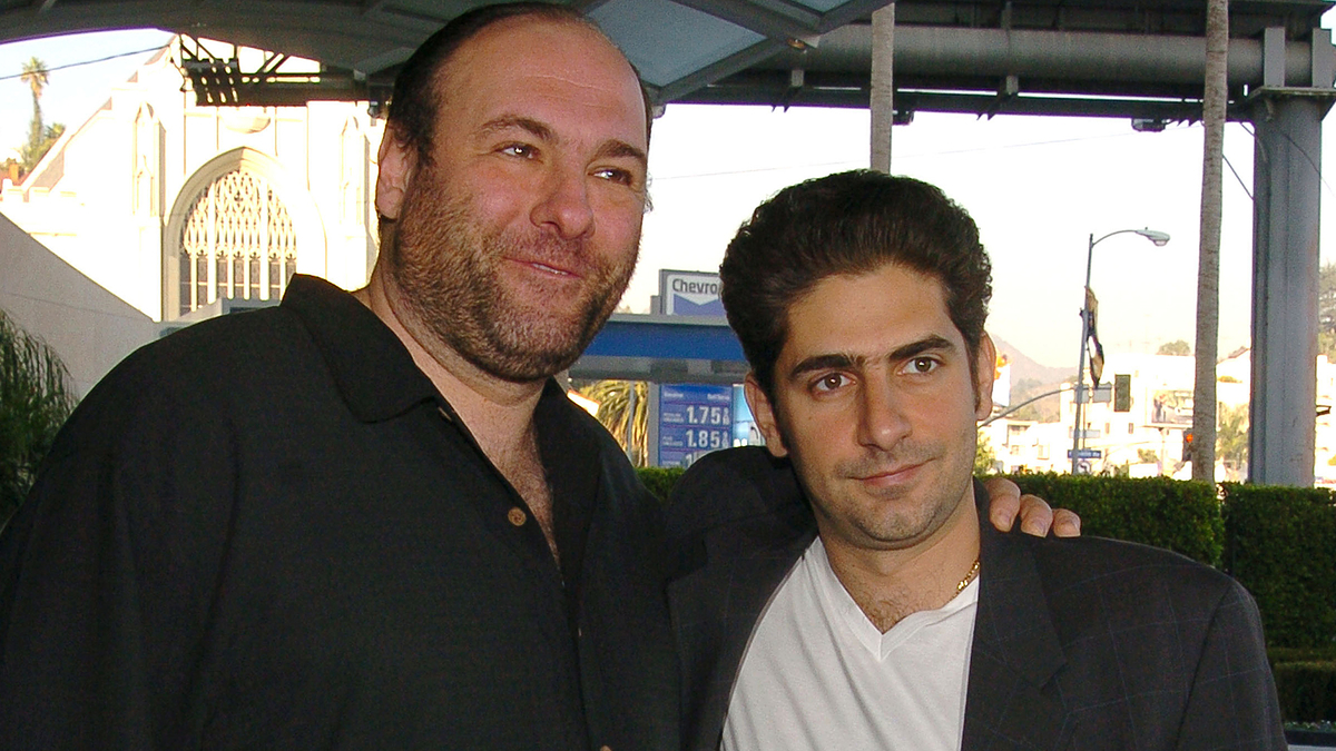 James Gandolfini and Michael Imperioli pose together outdoors, with Gandolfini in a black shirt and Imperioli in a white shirt and dark jacket