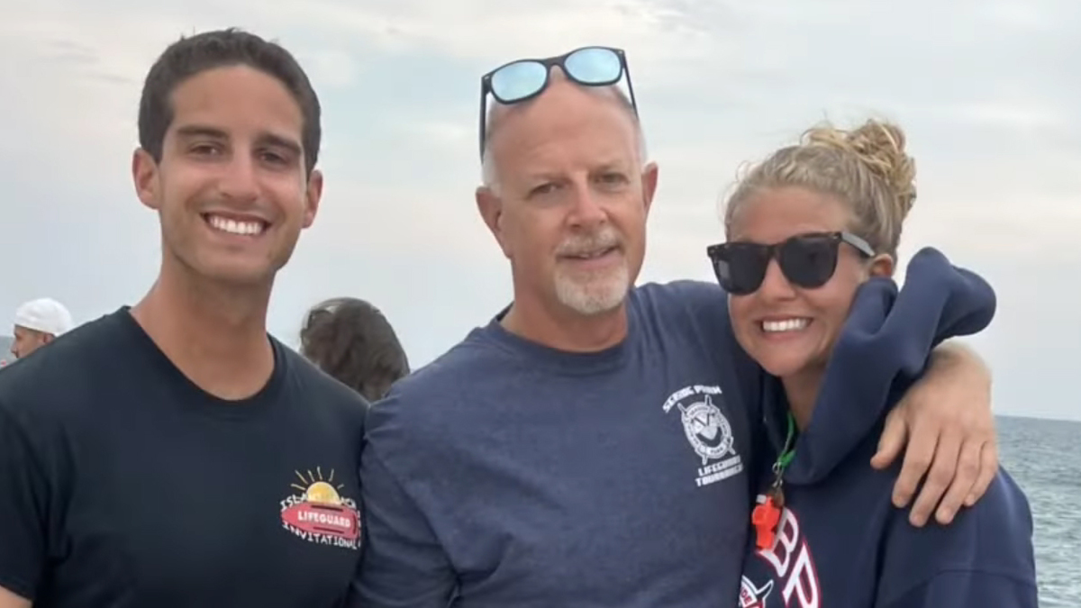 Three people, a young man in a t-shirt, an older man with glasses on his head, and a woman in a hoodie and sunglasses, standing together by the water. Names unknown