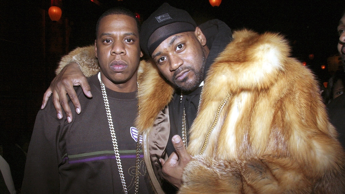 Jay-Z in a dark sweater and chain necklace, and Ghostface Killah in a fur coat and beanie, posing together with Jay-Z's arm around Ghostface Killah's shoulder