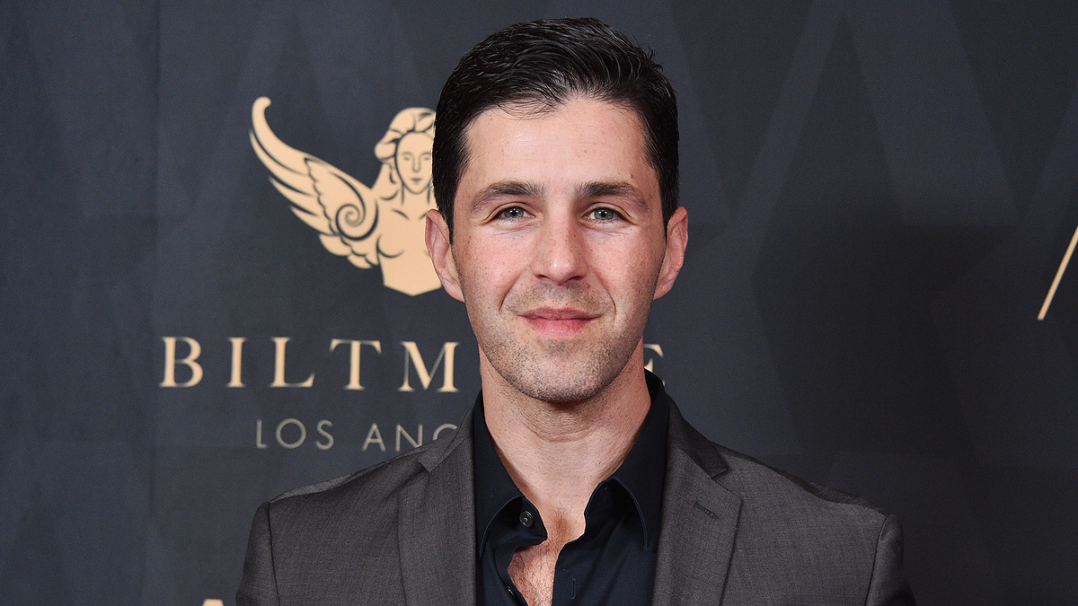 Josh Peck attends an event in Los Angeles, dressed in a formal dark suit jacket over a black shirt, with the Biltmore logo and name visible in the background