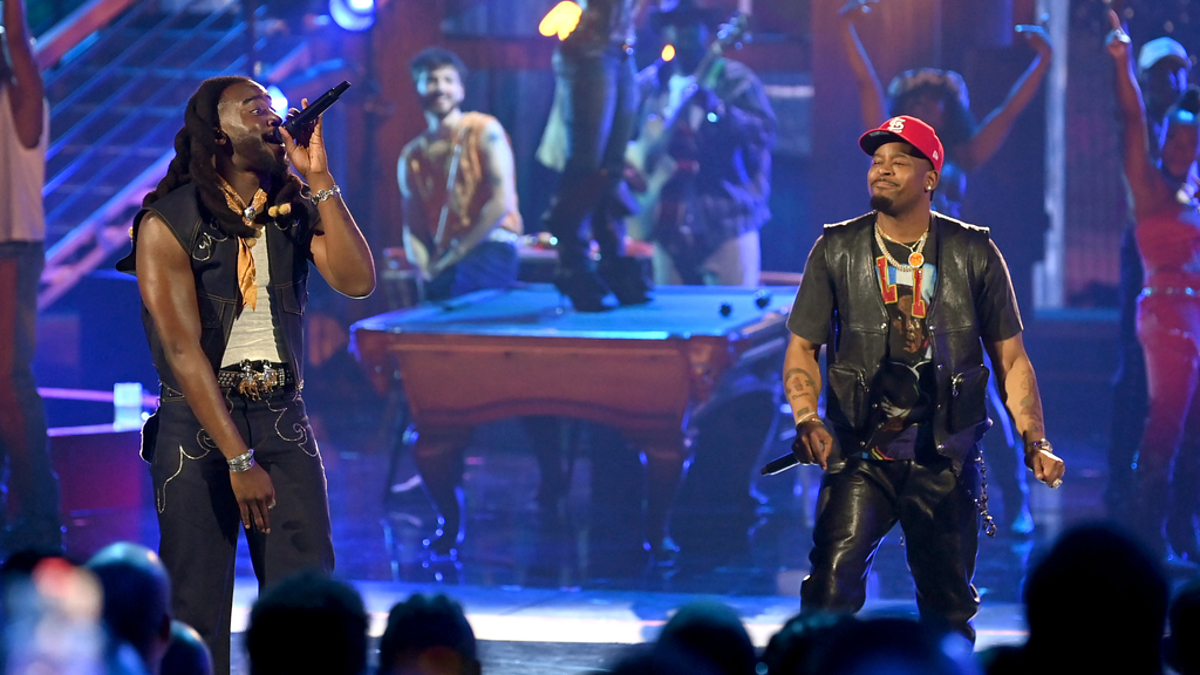 Dressed in black leather outfits, André 3000 and Big Boi of OutKast perform on stage with backup dancers and a lit background