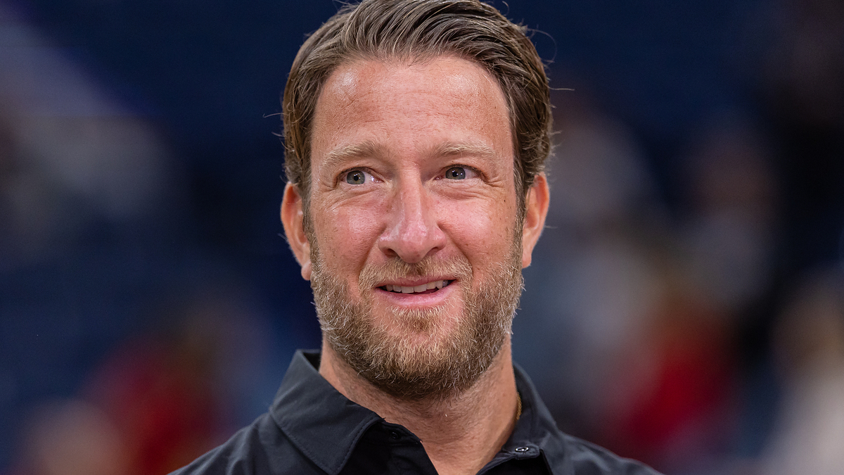 A man with short brown hair and a beard smiles while wearing a black button-up shirt