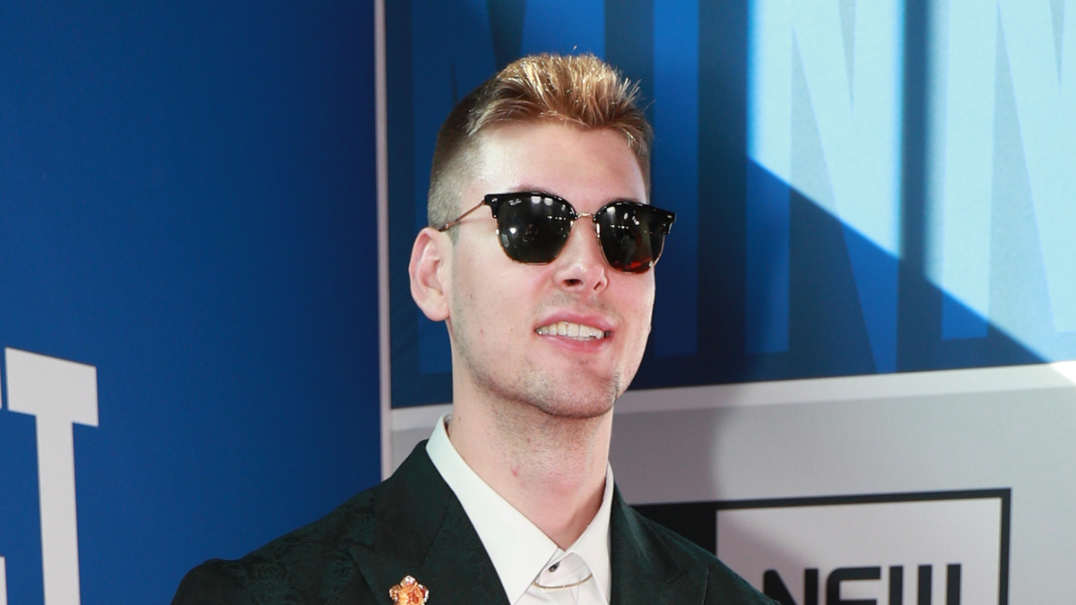 Man wearing sunglasses and a formal jacket with a lapel pin at an event