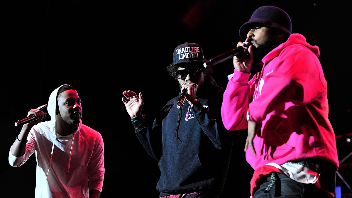 Kendrick Lamar, Ab-Soul, and Schoolboy Q perform on stage. Kendrick Lamar wears a hoodie, Ab-Soul wears sunglasses and a cap, and Schoolboy Q wears a beanie