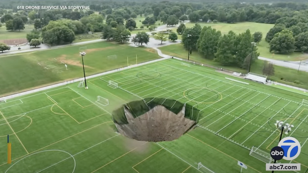 A drone photo shows a large sinkhole in the middle of an athletic field with soccer and lacrosse markings, reported by ABC 7 News