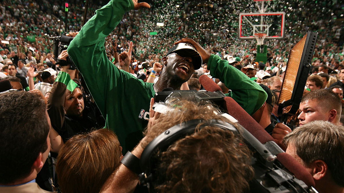 Basketball player celebrates victory on the court surrounded by fans and media, with confetti falling in the background