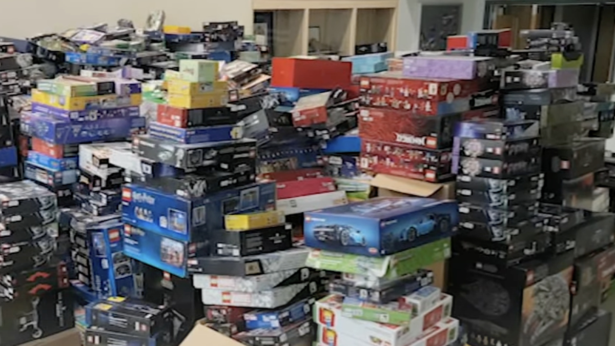 A room filled with stacks of various boxed LEGO sets with themes such as cars, architecture, and more, arranged in towering piles