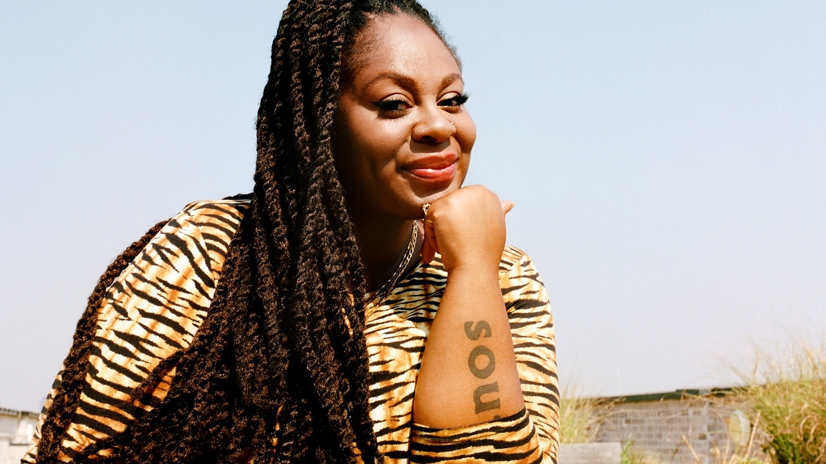 I don't know who is in the image. The woman is posing outdoors with her chin resting on her hand, displaying a "soul" tattoo on her arm and wearing a tiger-striped outfit