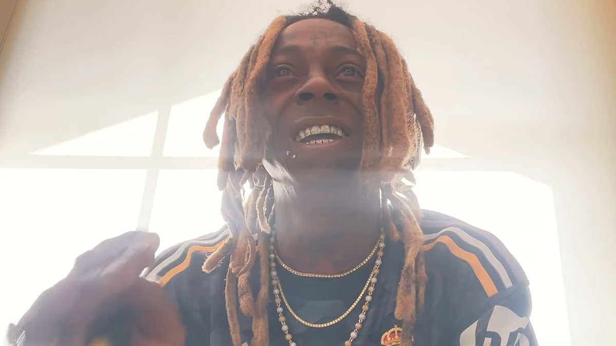 Lil Wayne smiling, wearing a sports jersey with gold necklaces and his signature dreadlocks