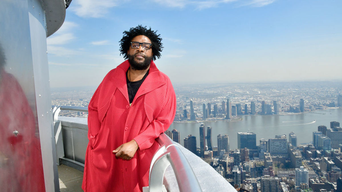 Man standing on a high balcony overlooking a cityscape that includes a river and tall buildings