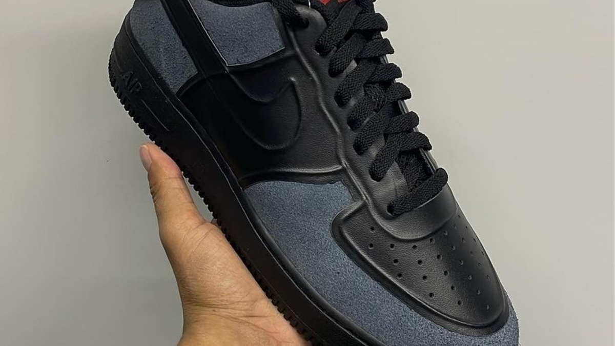 Close-up of a hand holding a black and gray Nike Air Force 1 sneaker with a price tag attached to it