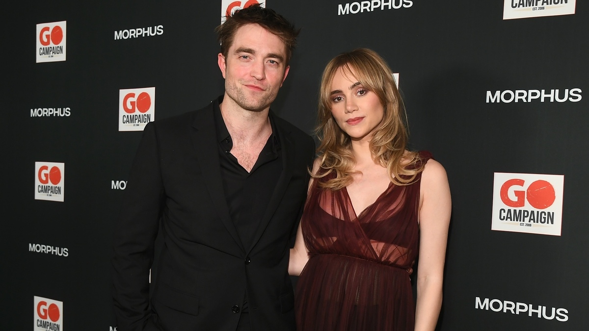 Robert Pattinson, in a black suit, and Suki Waterhouse, in an elegant sleeveless dress, pose together at a GO Campaign event