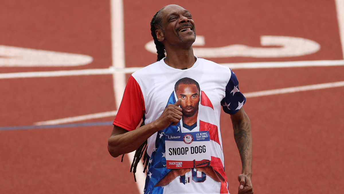 Snoop Dogg celebrates on a track, wearing a shirt featuring Kobe Bryant’s image draped in an American flag