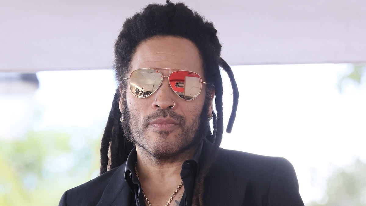 Lenny Kravitz wears sunglasses and a black jacket, looking forward