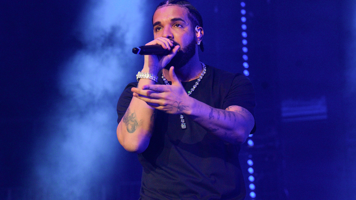 Drake performs on stage, holding a microphone and wearing a black outfit during a concert