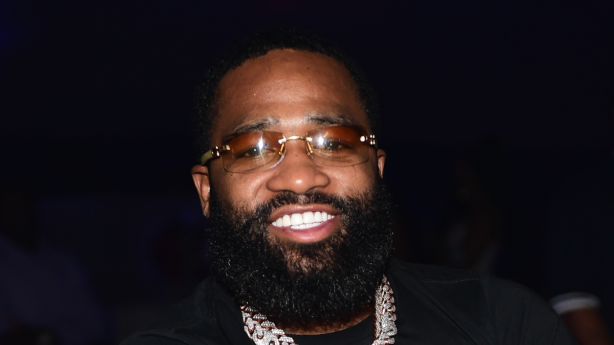 A bearded man with glasses and a necklace smiles at the camera