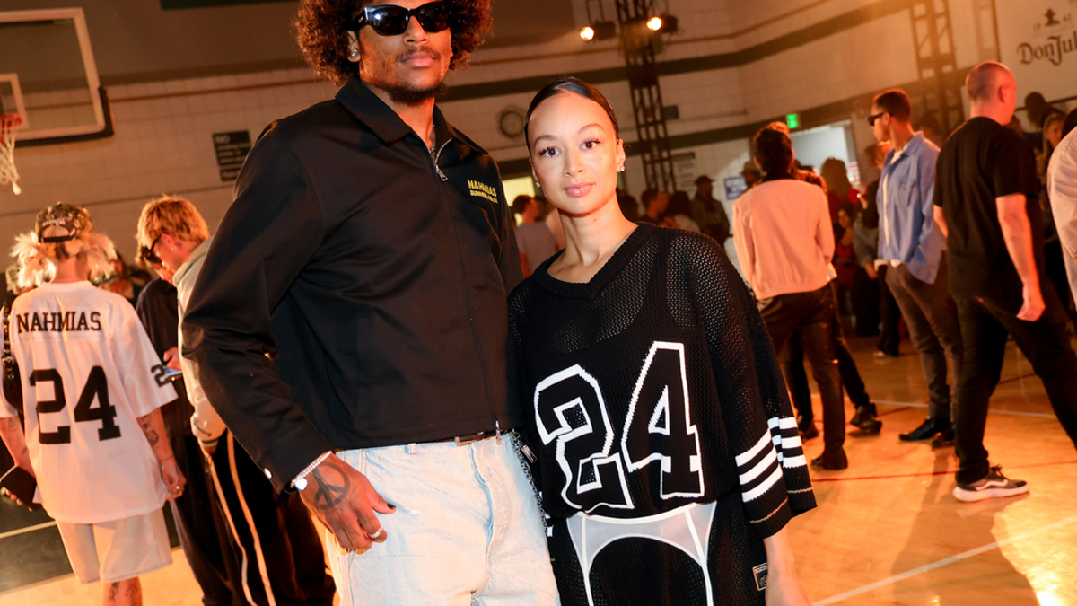 Kevin Porter Jr. and Draya Michele at a fashion event. Kevin wears a black shirt and jeans, while Draya wears a black sports jersey with the number 24