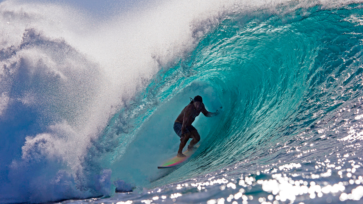 A person is surfing inside a large wave, maintaining balance on a surfboard with one arm outstretched
