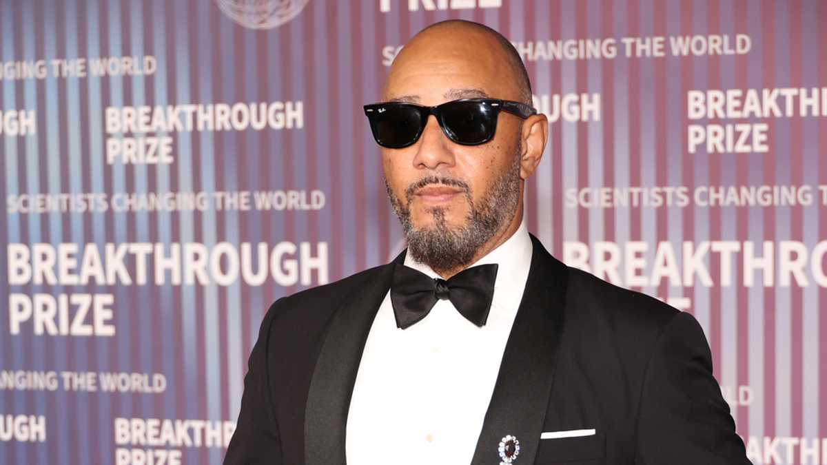 Swizz Beatz, wearing a black tuxedo with a bow tie and sunglasses, poses on the red carpet at the Breakthrough Prize event