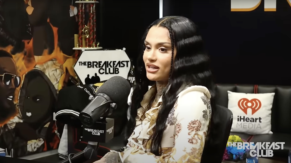 Kehlani speaks into a microphone during an interview at The Breakfast Club radio show. iHeartMedia and The Breakfast Club logos are visible in the background