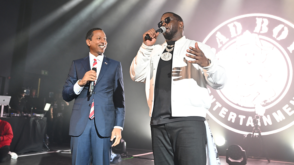 Rodney Ellis in a suit and sunglasses shares a stage with Sean ‘Diddy’ Combs, who is dressed casually and speaking into a microphone