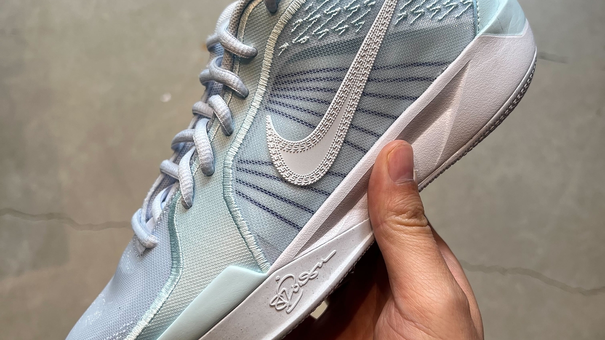 A hand holds a Nike sneaker with a sleek design and distinct Nike logo on the side